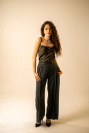 Woman wearing a black sleeveless top and high-waisted pants against a beige background