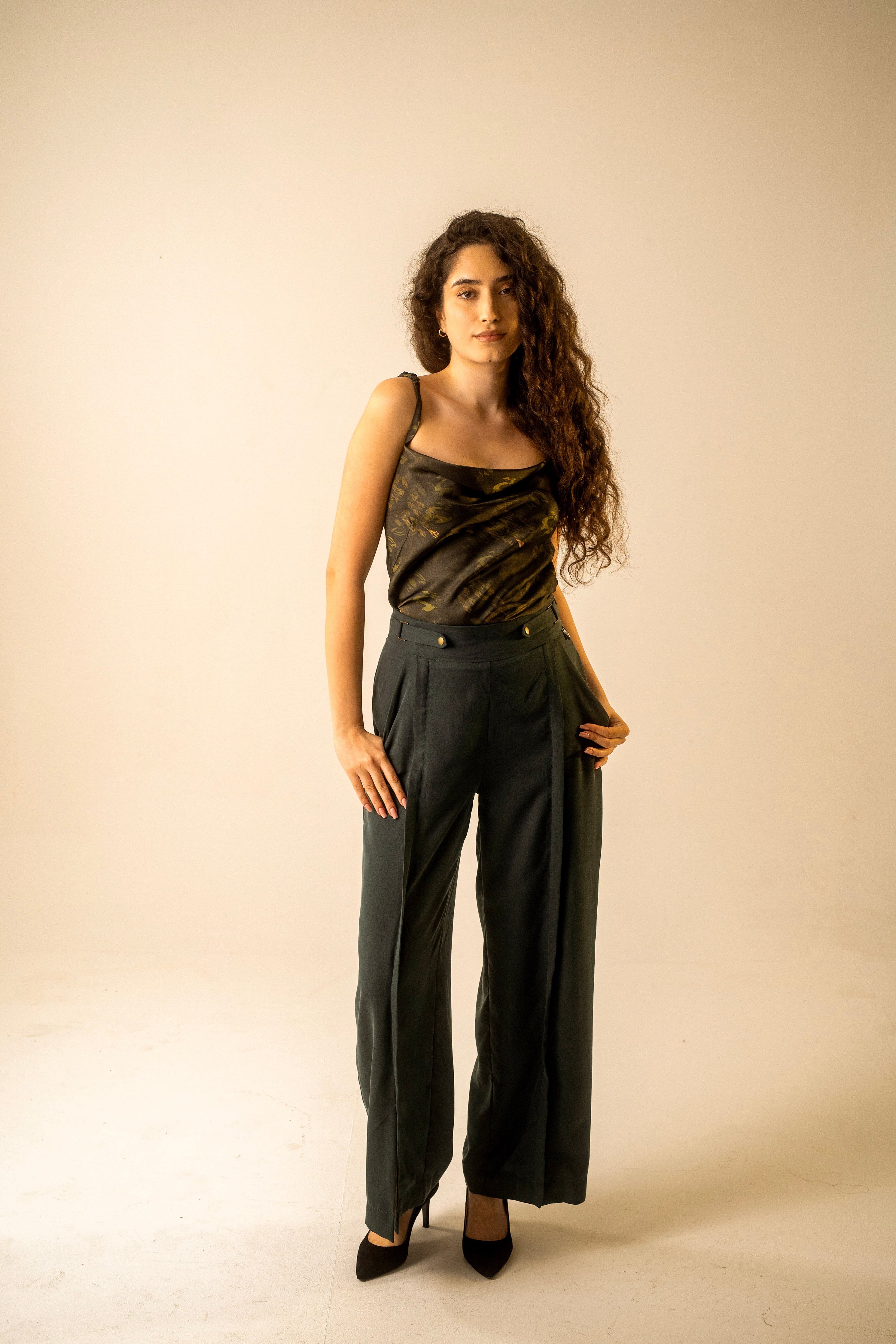 Woman wearing a black sleeveless top and high-waisted pants against a beige background